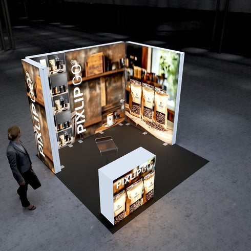 A bird’s-eye view of the Pixlip GO exhibition booth. The booth has a U-shaped layout with three illuminated walls and a centrally placed counter. The walls feature images of coffee beans, jars, and packaging in a warm, inviting design. A person is approaching the booth.