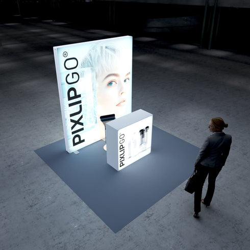 A sleek Pixlip GO exhibition booth with a large illuminated panel featuring a close-up image of a person with striking blue eyes and white-blonde hair. The counter in front displays minimalistic graphics of transparent bottles, matching the clean and modern theme. A person stands nearby observing the setup.