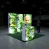 A side-angle view of the Pixlip GO booth emphasizing the interplay of green nature and technology. The main panel displays a woman with a circuit board, and the side and counter panels continue the theme with detailed visuals of circuit boards and greenery. A person walks toward the booth.