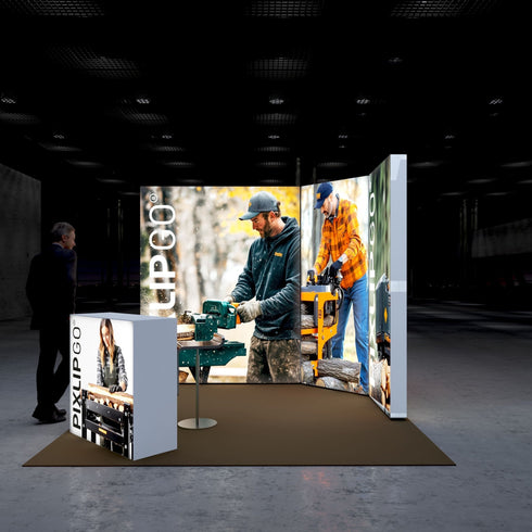 A side view of the Pixlip GO booth emphasizing its rustic and hands-on woodworking theme. The backdrop displays men using woodworking tools, while the front counter highlights a woman engaged in crafting. A person stands at a distance, observing the setup.