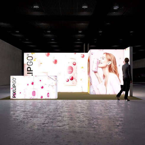 A frontal view of the Pixlip GO booth showcasing its playful and fresh theme. The large illuminated backdrop features colorful images of cherries, beverages, and a cheerful woman sipping from a drink can. The counter complements the visuals with a similar bright and fruity design.