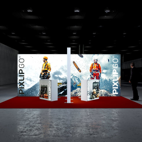 A frontal view of the Pixlip GO booth showcasing its theme of extreme conditions and safety equipment. The large backdrop displays mountaineers in vibrant orange gear scaling snowy mountains. Two counters with industrial tool displays complement the visuals, placed on a bold red carpet.