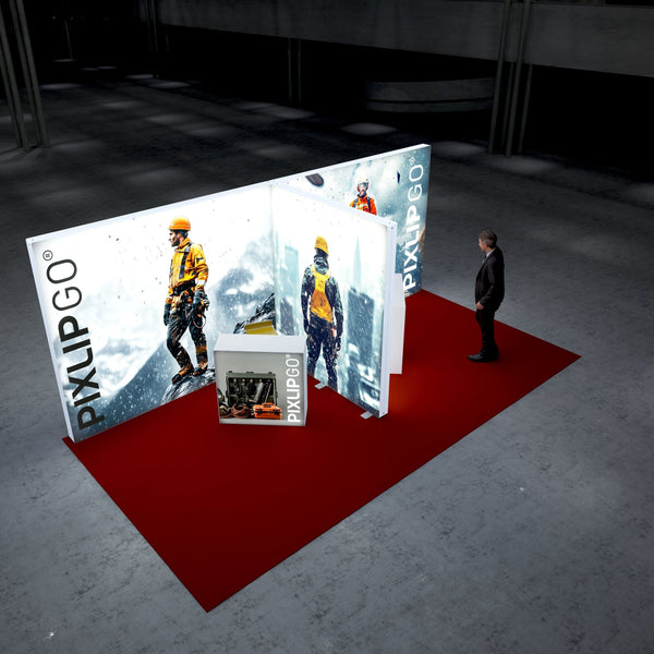 A Pixlip GO exhibition booth with a rugged and adventurous theme. The illuminated panels feature images of mountaineers equipped with safety gear, set against a snowy mountain landscape. A front counter displays industrial tools in a case. A visitor stands nearby, observing the booth.