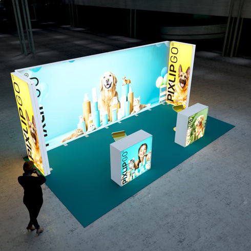 A Pixlip GO exhibition booth with a vibrant pet care theme. The illuminated panels display playful images of cats, dogs, and pet care products against a bright blue background. The setup includes counters with matching pet-themed designs, while a visitor observes the booth from a distance.