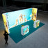 A Pixlip GO exhibition booth with a vibrant pet care theme. The illuminated panels display playful images of cats, dogs, and pet care products against a bright blue background. The setup includes counters with matching pet-themed designs, while a visitor observes the booth from a distance.
