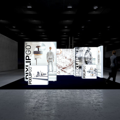A frontal view of the PIXLIPGO trade fair booth, illuminated with displays of mechanical engineering elements, including a CNC machine and industrial gear systems. A person in a suit stands to the left, adding scale to the exhibit.