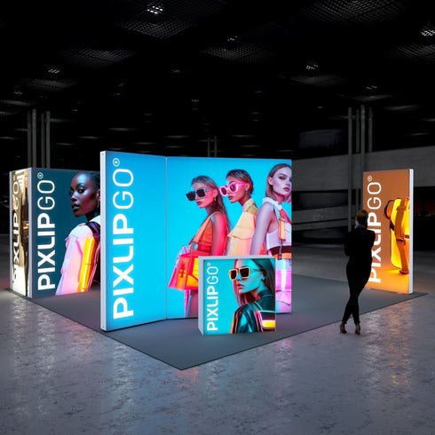 Side angle of an illuminated exhibition setup featuring vibrant displays of fashion models and luxury accessories. Central panels display trendy women in neon-colored outfits, complemented by smaller displays showcasing handbags and sunglasses.