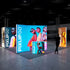Side angle of an illuminated exhibition setup featuring vibrant displays of fashion models and luxury accessories. Central panels display trendy women in neon-colored outfits, complemented by smaller displays showcasing handbags and sunglasses.
