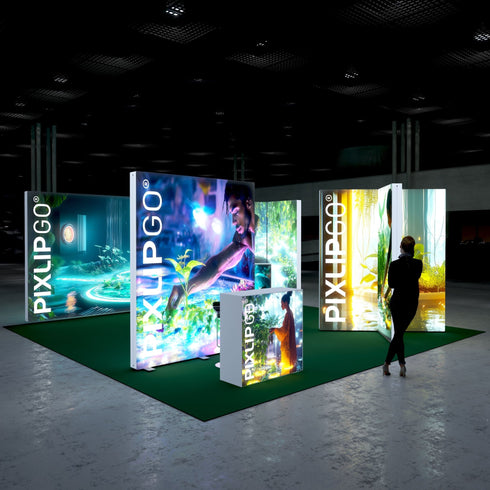 A side-angle view of the trade show setup, highlighting the illuminated lightboxes with detailed natural scenery and a glowing yellow accent panel. A woman is engaged with the booth, reflecting an interest in the environmental storytelling conveyed by the display