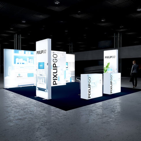 A spacious trade show booth with illuminated PIXLIP GO displays featuring medical and laboratory themes. The booth includes lighted counters and tall panels, creating a modern and clean design on a navy blue carpet.